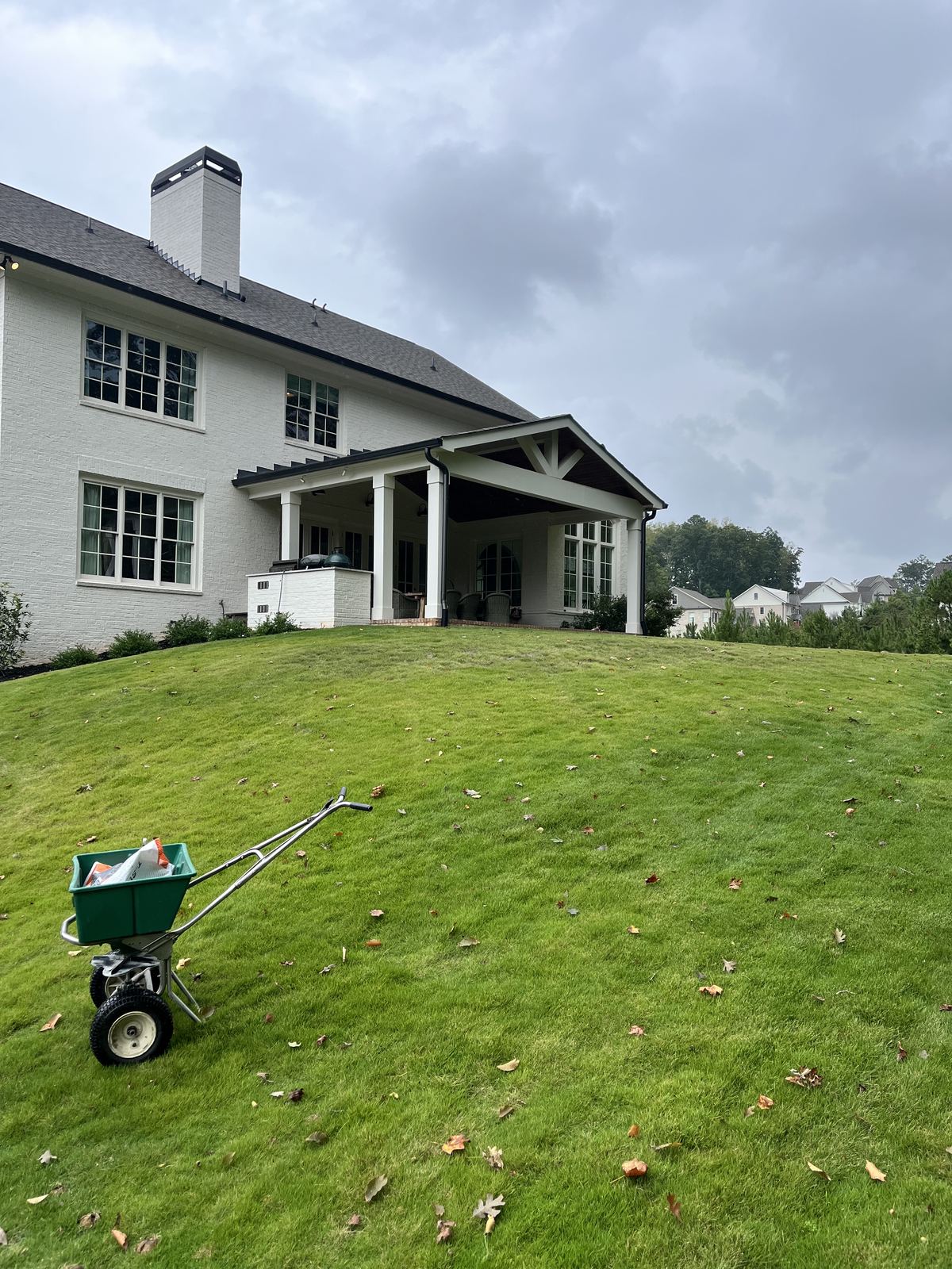 Fertilizer spreader on a green fescue lawn behind a white house